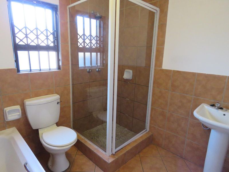 A functional bathroom featuring a shower enclosure, pedestal basin, and toilet with neutral tiled finishes and security bars on the window.