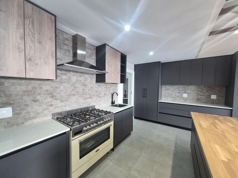 Modern kitchen featuring dark cabinetry, wood-tone accents, stone countertops, a gas stove with extractor fan, and a tiled backsplash.
