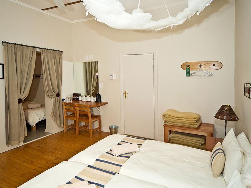 A hotel bedroom featuring hardwood flooring, a ceiling fan, and an adjoining space, offering a functional and comfortable layout for guests.