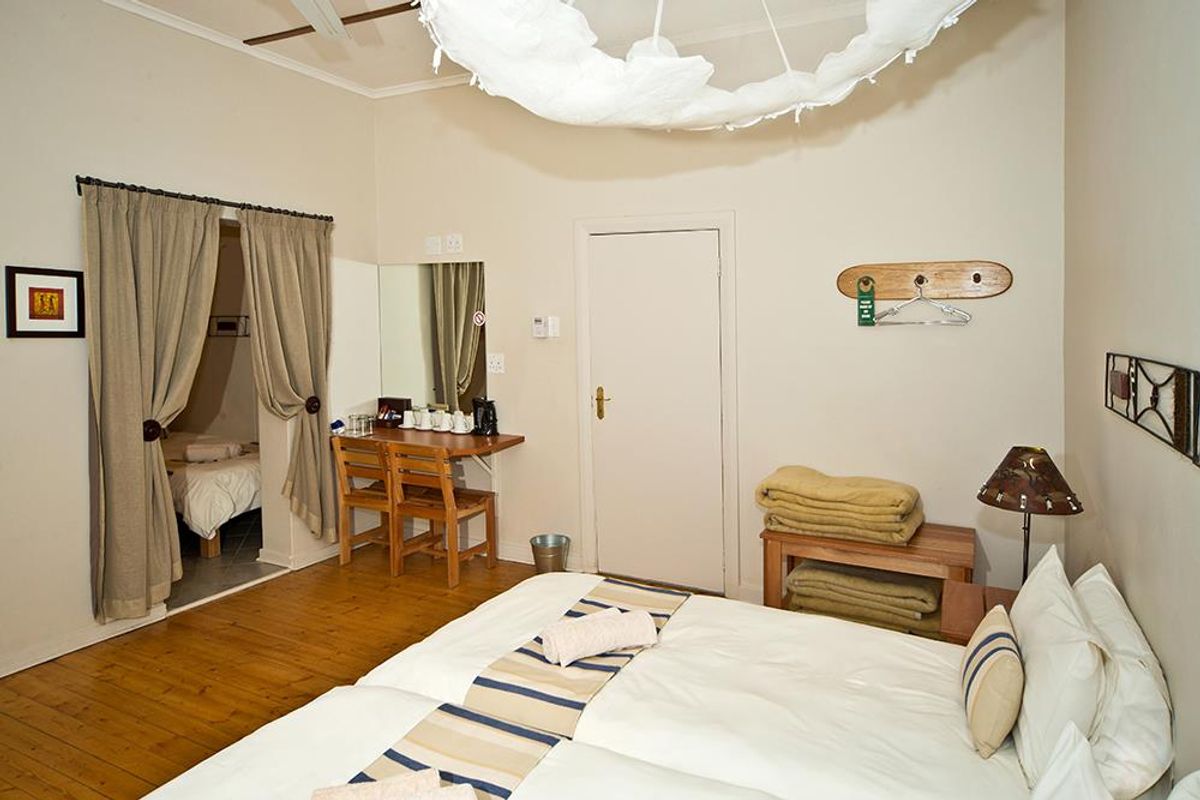 A hotel bedroom featuring hardwood flooring, a ceiling fan, and an adjoining space, offering a functional and comfortable layout for guests.