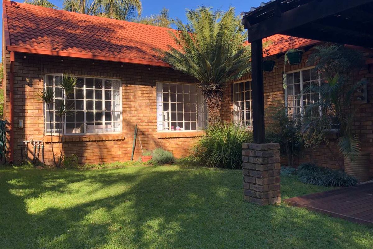 Rear view of the house featuring a face brick facade, terracotta roof tiles, and a timber pergola overlooking a well-maintained garden.