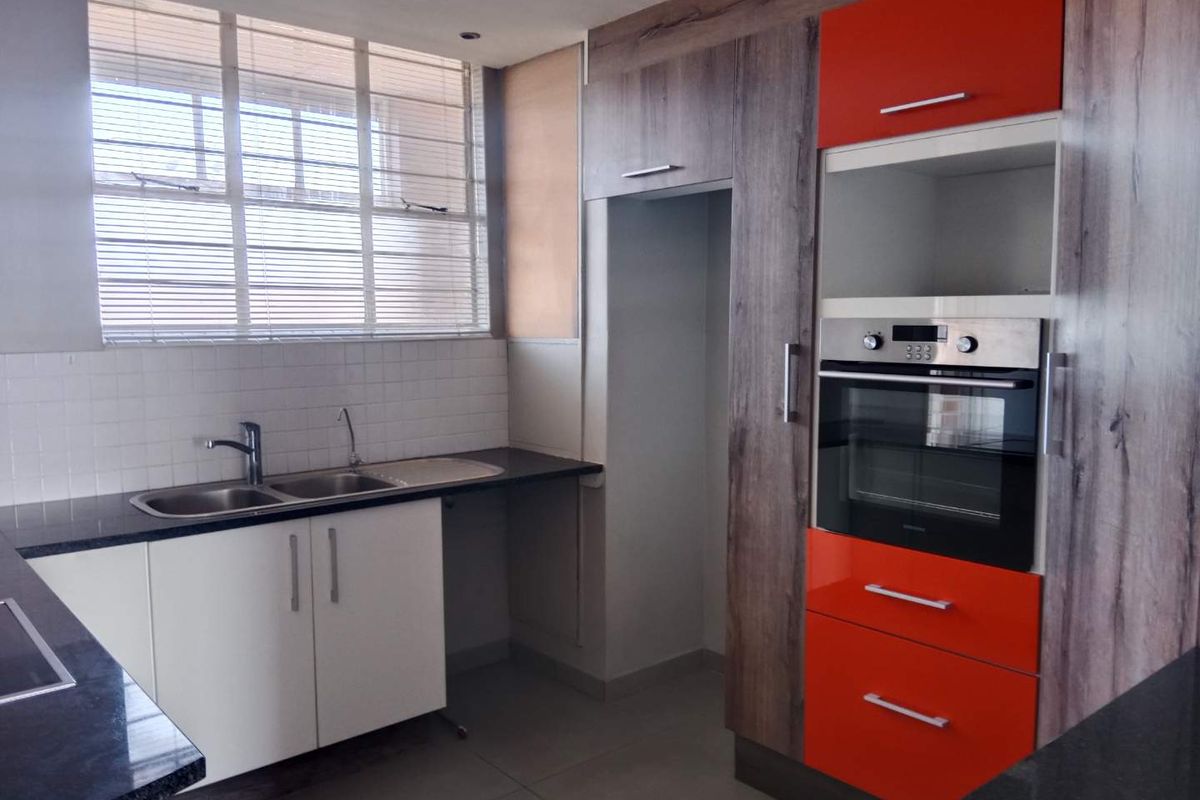 A modern kitchen featuring high-contrast orange and wood-grain cabinetry, granite countertops, a built-in oven, and a double sink with a tiled backsplash.