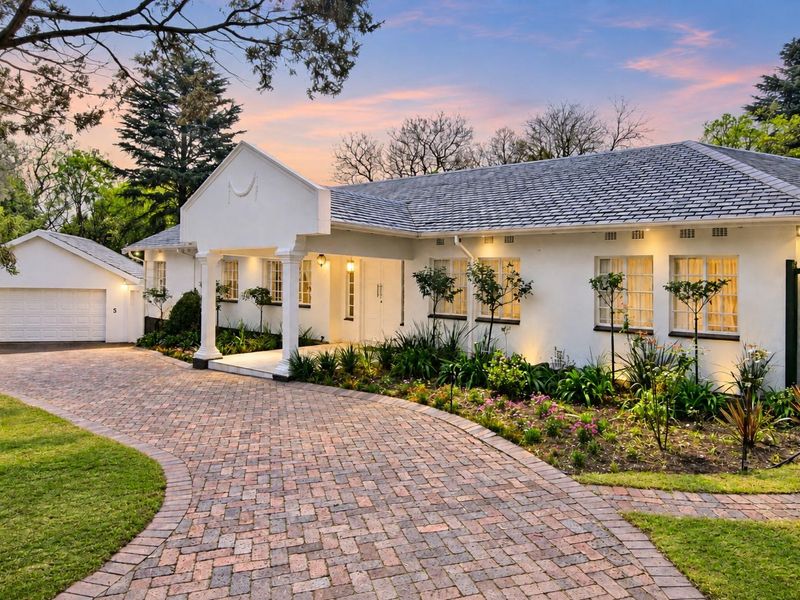 A beautifully maintained single-story residence featuring a classic white facade, a grand covered entrance, a brick-paved driveway, and a detached garage.