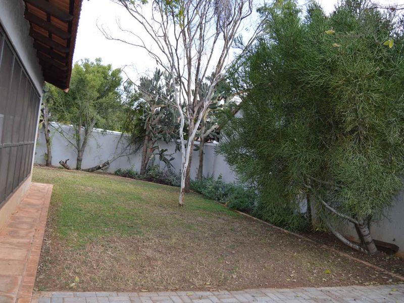 A private rear garden area featuring a lawn, mature trees, boundary walls, and access to a screened patio enclosure.