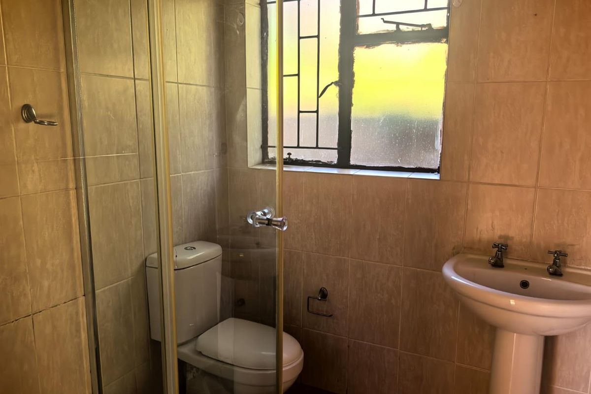 A functional bathroom featuring a pedestal basin, toilet, and shower enclosure with tiled walls and security bars on the window.