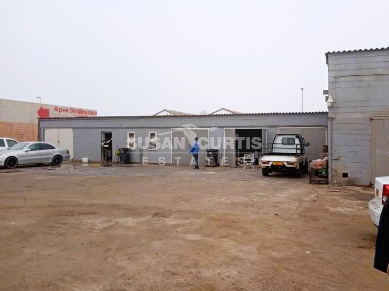 Industrial property exterior featuring multiple roller door access points, concrete block construction, and a large open yard area suitable for commercial or workshop use.