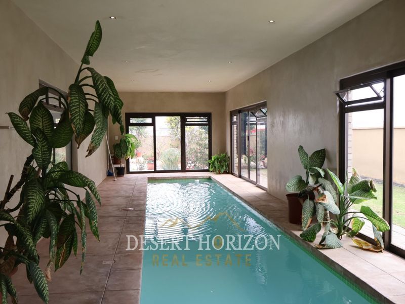 An indoor swimming pool area featuring tiled flooring, recessed lighting, and large sliding glass doors providing views of the garden.