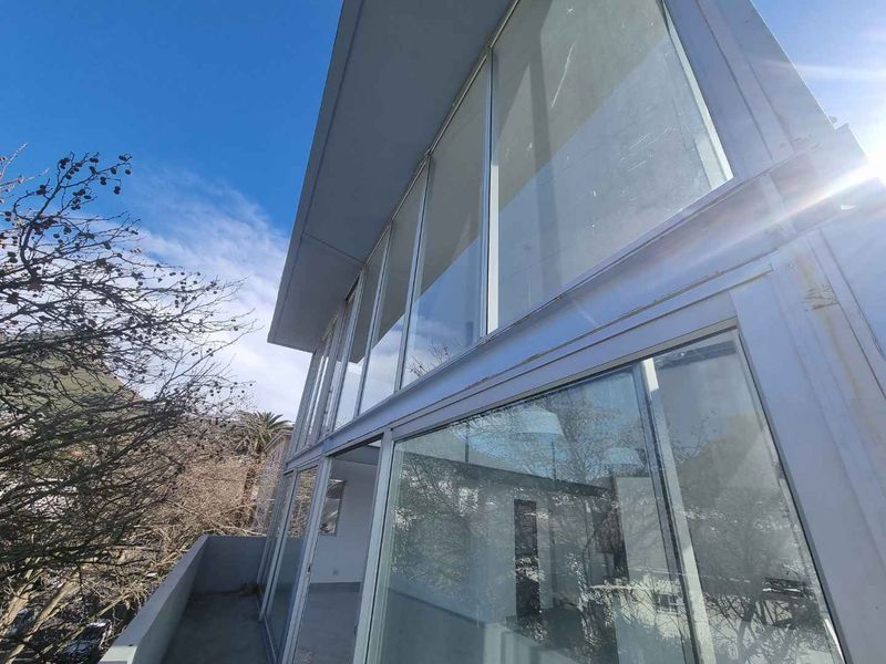 Exterior view of the penthouse featuring floor-to-ceiling glass windows and a concrete balcony, showing signs of weathering on the metal frames.
