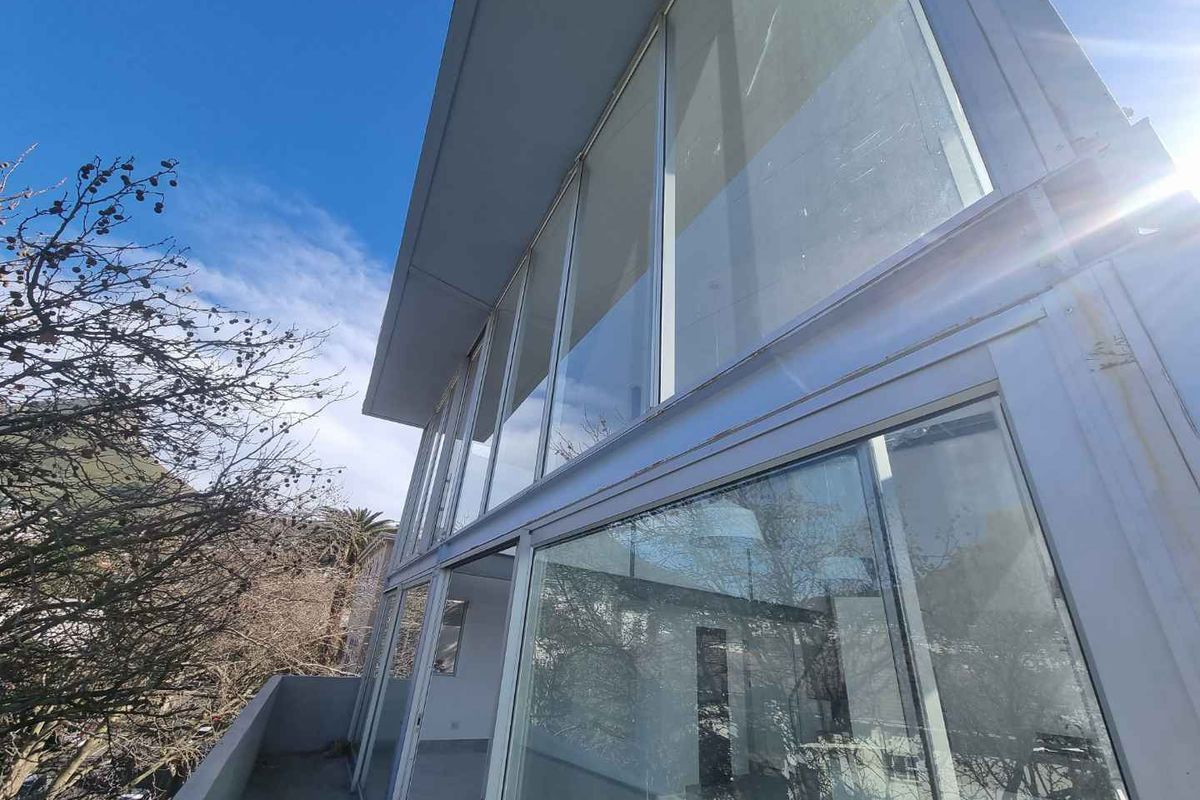 Exterior view of the penthouse featuring floor-to-ceiling glass windows and a concrete balcony, showing signs of weathering on the metal frames.