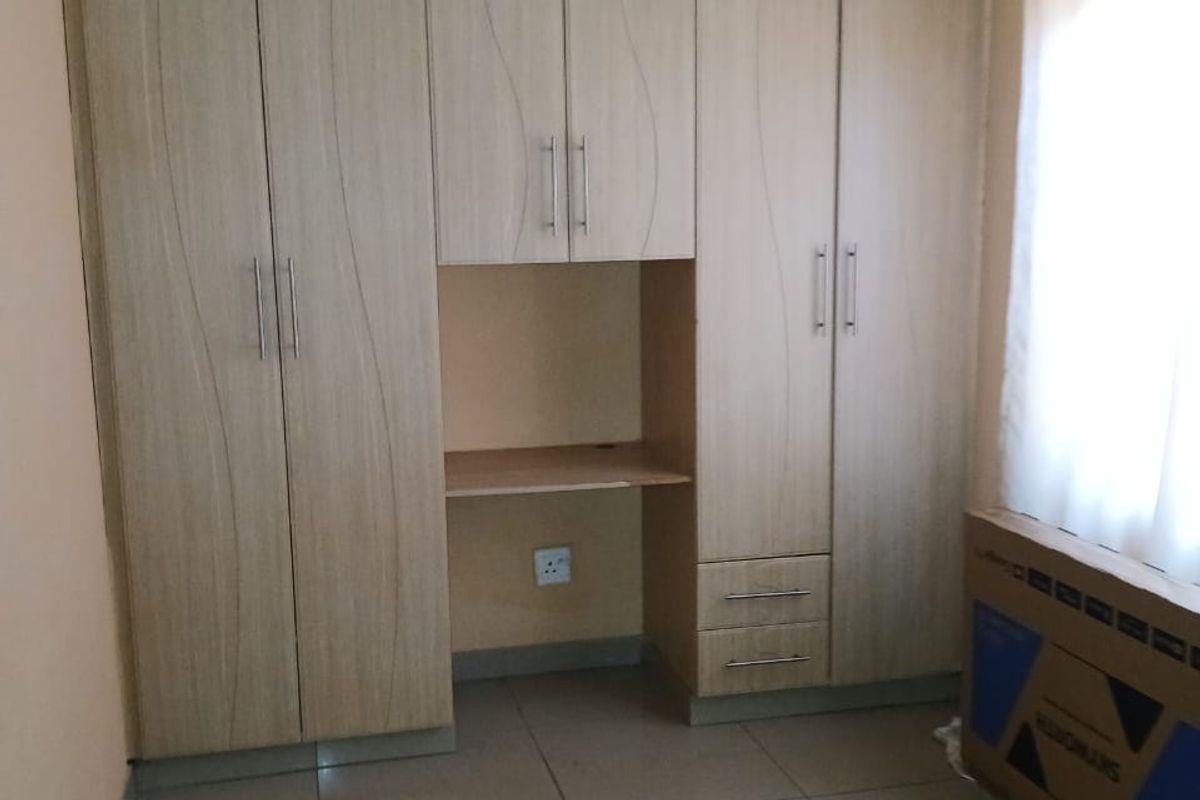 A bedroom featuring built-in wooden cupboards with an integrated desk area, tiled flooring, and a neutral color palette.