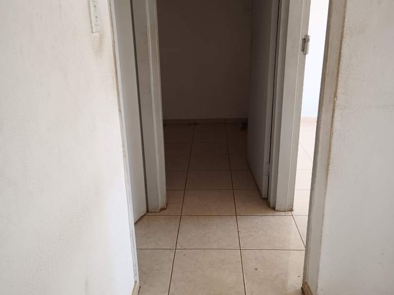 A vacant hallway featuring neutral ceramic floor tiles and plain white walls, showing signs of wear and requiring cosmetic updates.