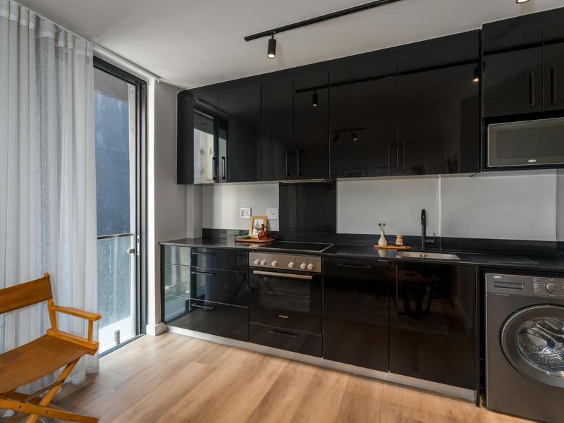 Modern kitchen featuring sleek black high-gloss cabinetry, integrated appliances, electric hob, built-in oven, and durable laminate flooring with direct access to a balcony.