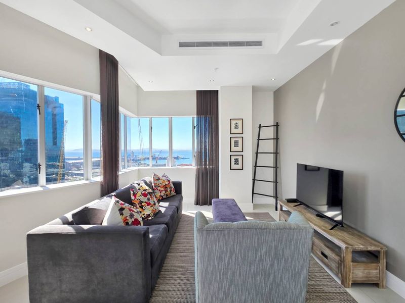 A bright, modern living room featuring recessed ceilings, ducted air conditioning, and expansive windows offering panoramic city and harbor views.