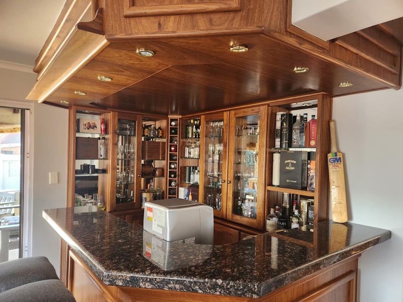 A well-maintained built-in wooden bar area featuring a granite countertop, integrated glass display cabinetry, and recessed ceiling lighting.