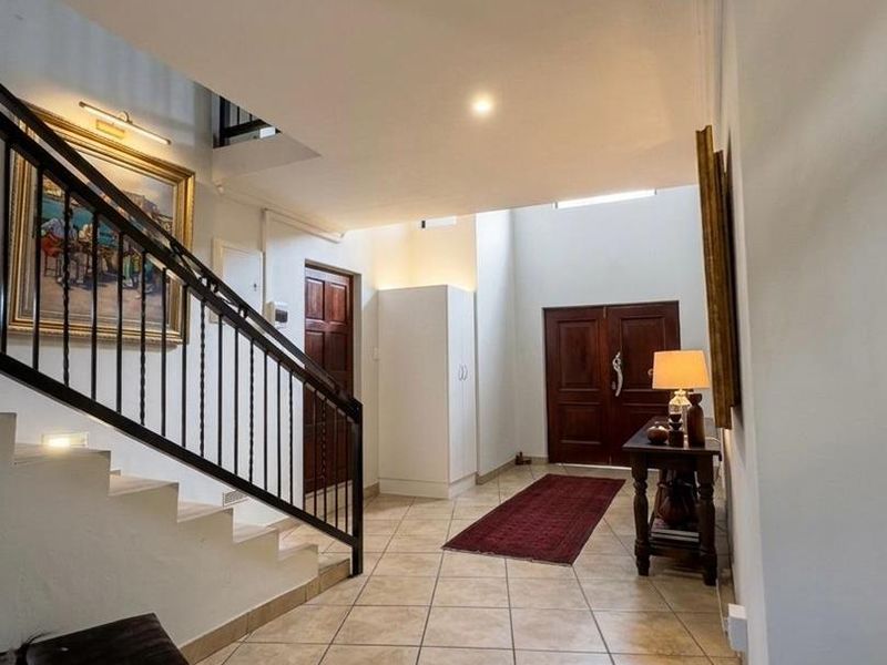 Spacious entrance hall featuring tiled flooring, a staircase with a wrought iron balustrade, and double front doors.