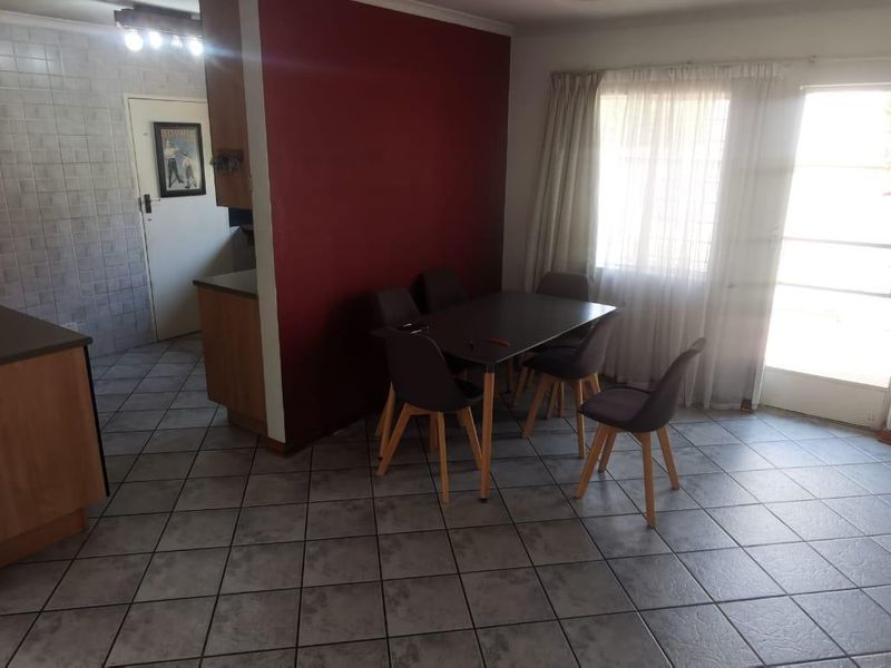 Open-plan living and dining area featuring tiled flooring, built-in kitchen cabinetry, and direct access to the exterior via a security gate.