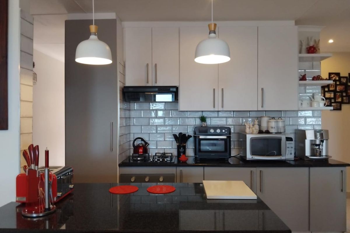 Modern kitchen featuring sleek cabinetry, subway tile backsplash, dark granite countertops, and a functional island with integrated lighting.