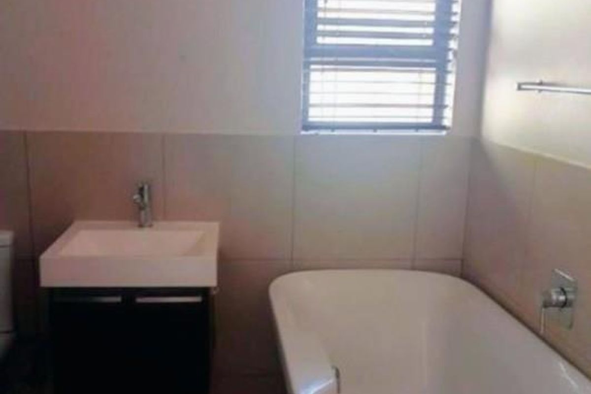 A clean, modern bathroom featuring a wall-mounted vanity, a white bathtub, tiled finishes, and a window with fitted blinds.