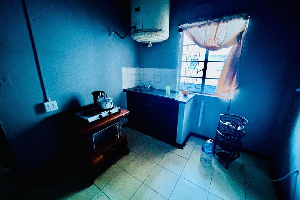 A compact kitchen area featuring a basic sink unit, wall-mounted water heater, and tiled flooring, requiring significant modernization and repair.