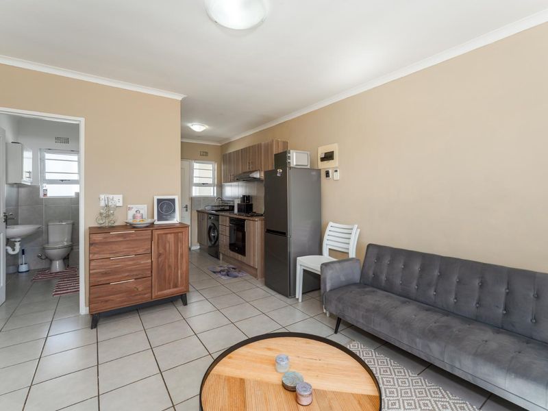 Open-plan living area featuring tiled floors, a compact kitchen with built-in cabinetry and appliances, and direct access to an adjacent bathroom.
