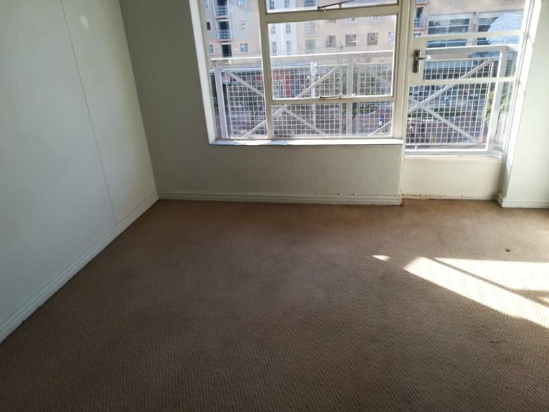 An empty bedroom featuring carpeted flooring, a large window, and a security gate leading to an exterior balcony area.