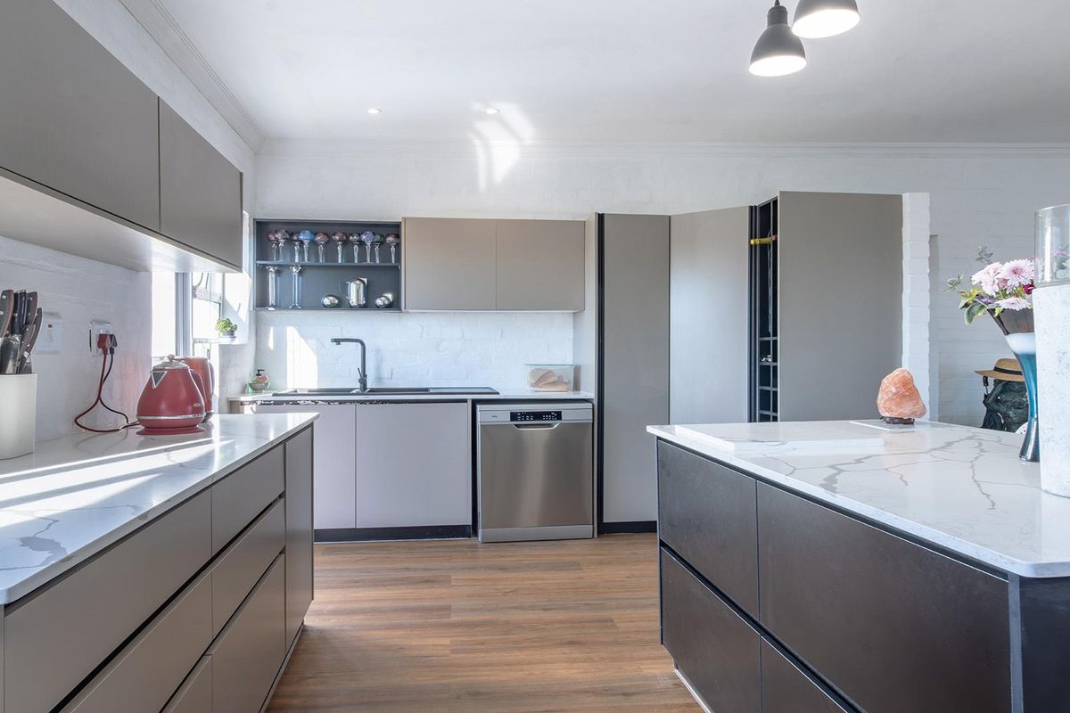Modern kitchen featuring sleek grey cabinetry, stone countertops, a central island, and integrated appliances, creating a clean and functional culinary space.