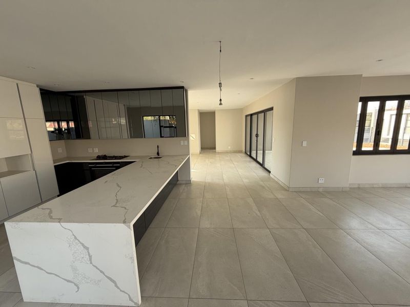 Modern open-plan kitchen and living area featuring a stone island, sleek cabinetry, tiled floors, and large sliding doors leading to the exterior.