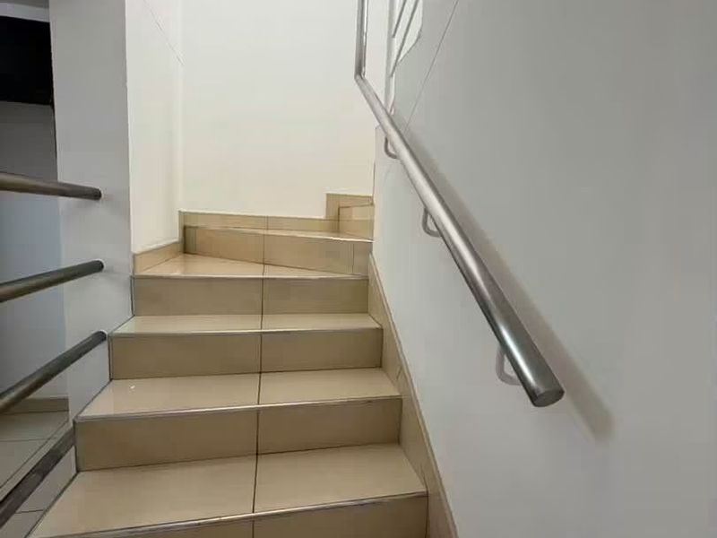 A clean, modern staircase featuring neutral floor tiles, a stainless steel handrail, and a matching metal balustrade.