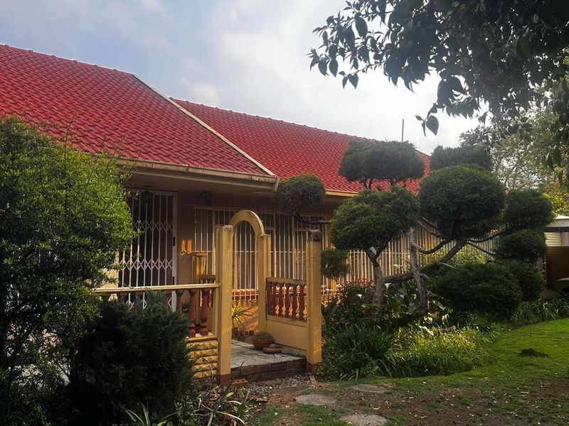 Front elevation of a house featuring a red tiled roof, security gates, and a well-maintained garden with a paved entrance path.