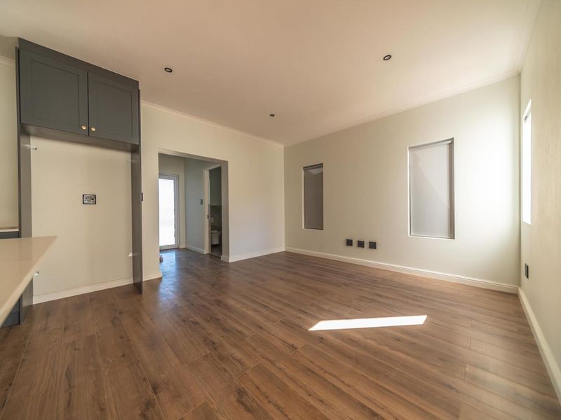 A bright, open-plan living area featuring modern laminate flooring, recessed lighting, and built-in cabinetry with a stone countertop.