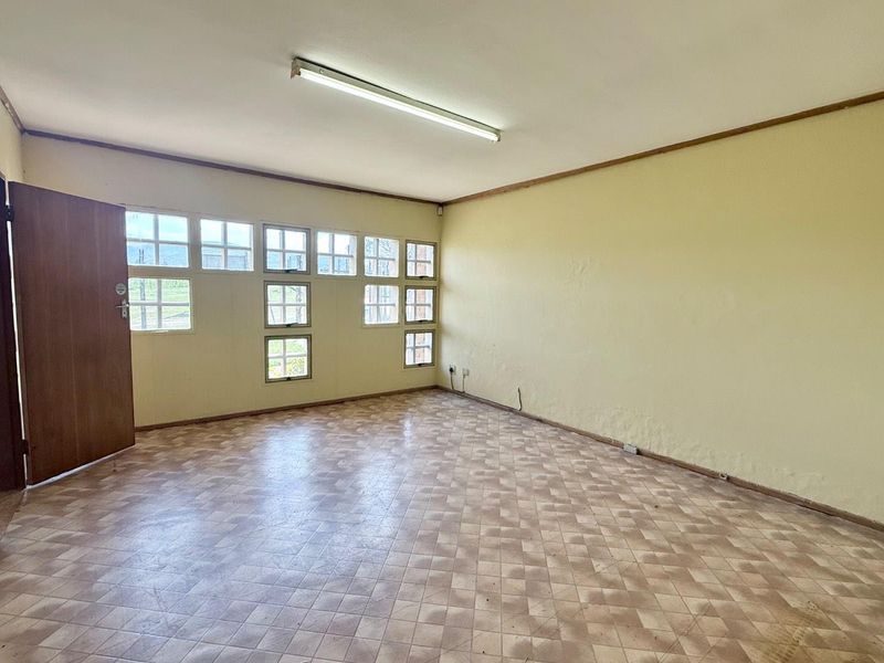 An empty office space featuring vinyl tile flooring, grid windows, and fluorescent lighting, suitable for a professional workspace.