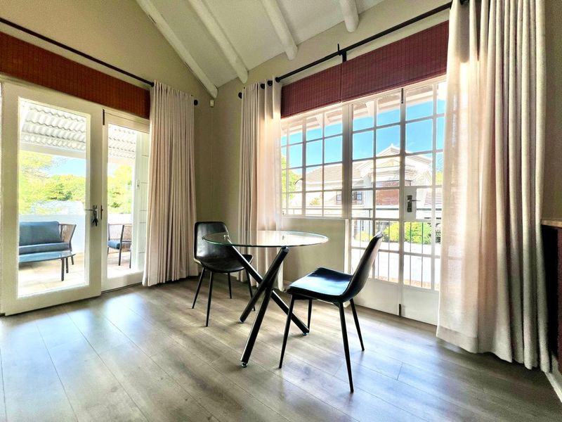 Bright living area featuring vaulted ceilings with exposed rafters, laminate flooring, and multiple sets of french doors providing access to the outdoor patio.