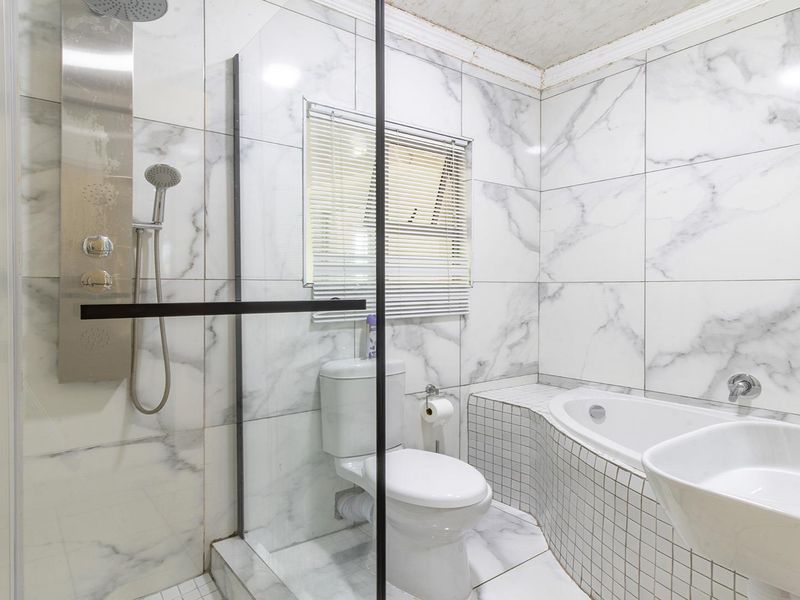 Modern bathroom featuring marble-look wall tiles, a glass shower enclosure with a built-in shower panel, and a tiled bathtub surround.