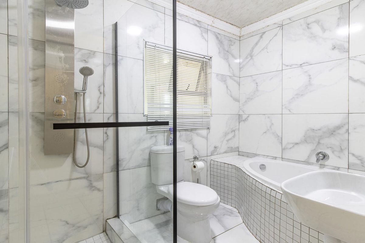 Modern bathroom featuring marble-look wall tiles, a glass shower enclosure with a built-in shower panel, and a tiled bathtub surround.