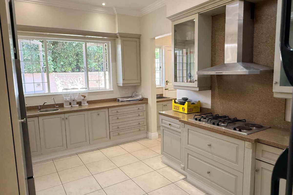 A well-maintained kitchen featuring neutral cabinetry, stone countertops, a gas hob with stainless steel extractor, and tiled flooring with ample natural light.