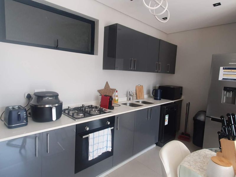 Modern kitchen featuring high-gloss grey cabinetry, stone countertops, a gas hob, and a built-in oven, offering a clean and contemporary aesthetic.