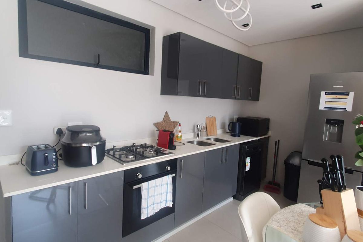 Modern kitchen featuring high-gloss grey cabinetry, stone countertops, a gas hob, and a built-in oven, offering a clean and contemporary aesthetic.