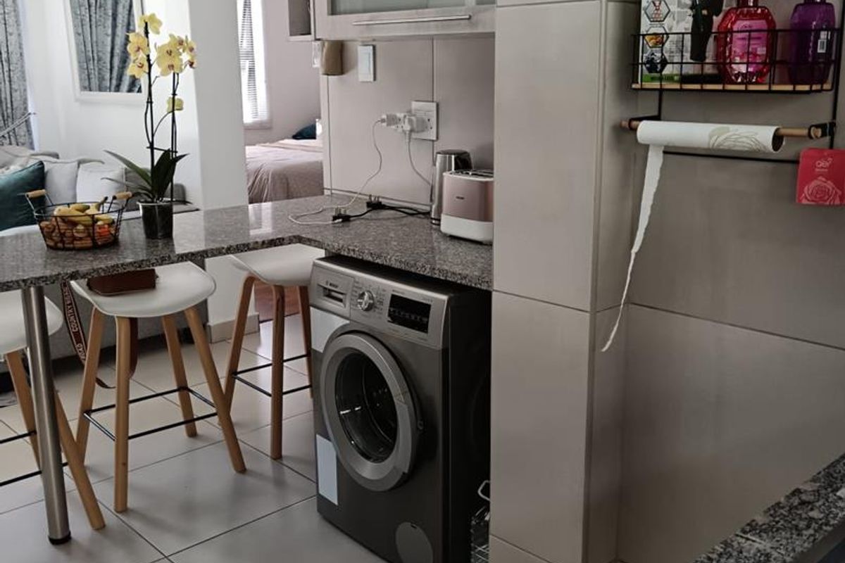 A functional kitchen area featuring granite countertops, built-in cabinetry, and an integrated washing machine, seamlessly connected to the living space.