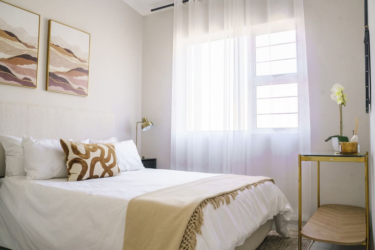 A well-lit bedroom featuring neutral tones, a large window with sheer curtains, and a clean, modern aesthetic.