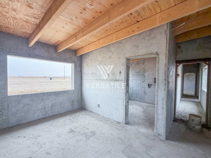 An unfinished bedroom space featuring exposed timber ceiling beams, raw concrete walls, and cement flooring, offering a blank canvas for custom interior finishes.