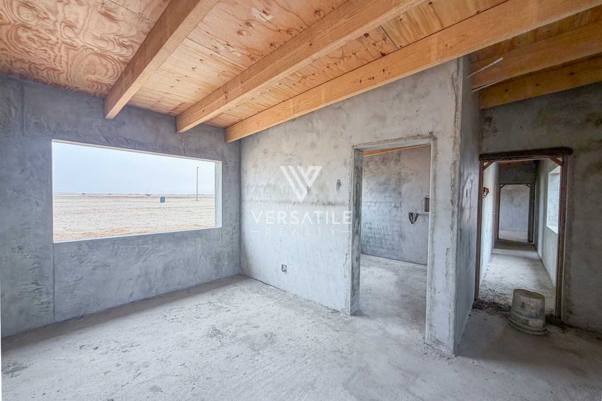 An unfinished bedroom space featuring exposed timber ceiling beams, raw concrete walls, and cement flooring, offering a blank canvas for custom interior finishes.