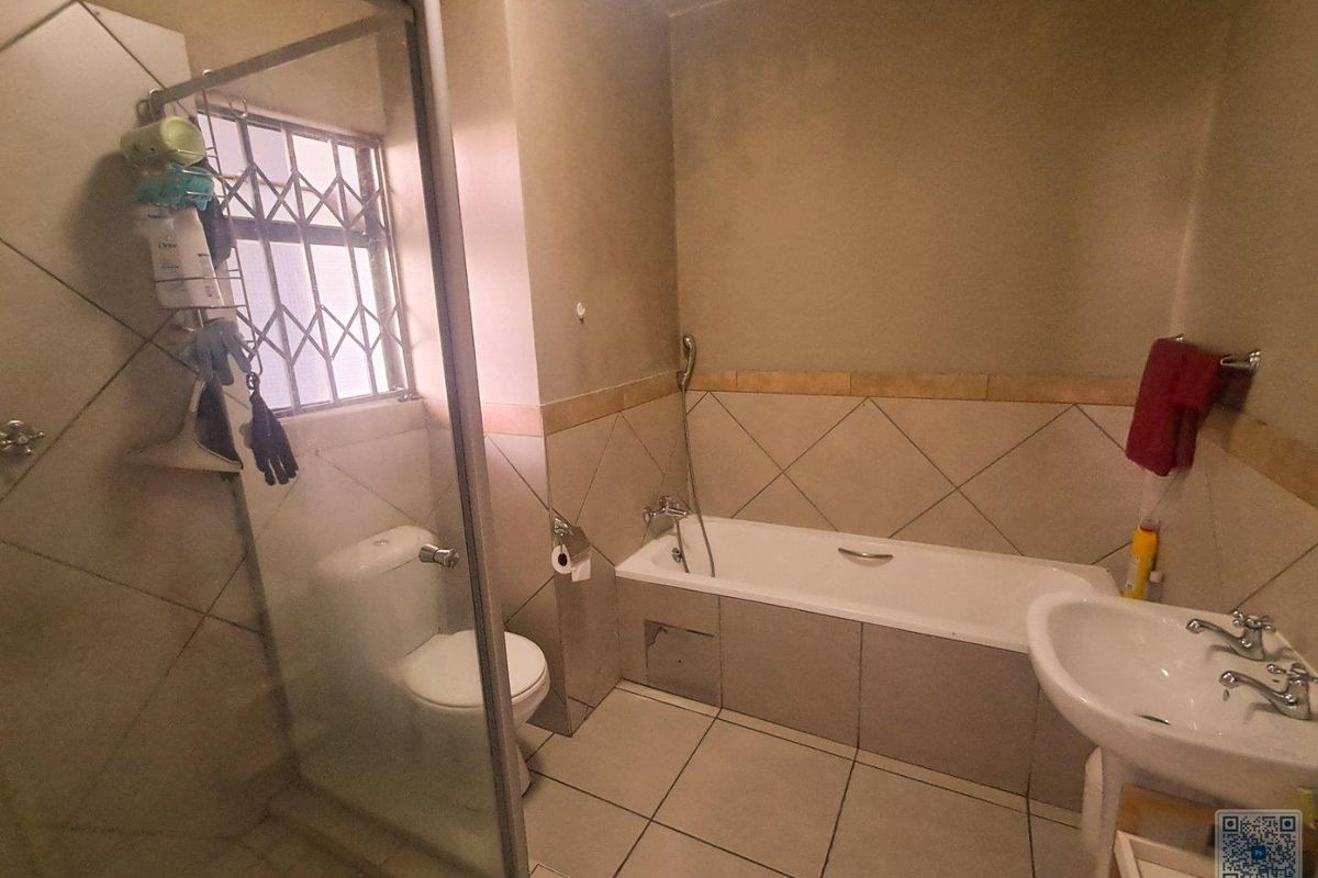 A functional bathroom featuring a bathtub, separate glass-enclosed shower, pedestal basin, and toilet with tiled flooring and partial wall tiling.