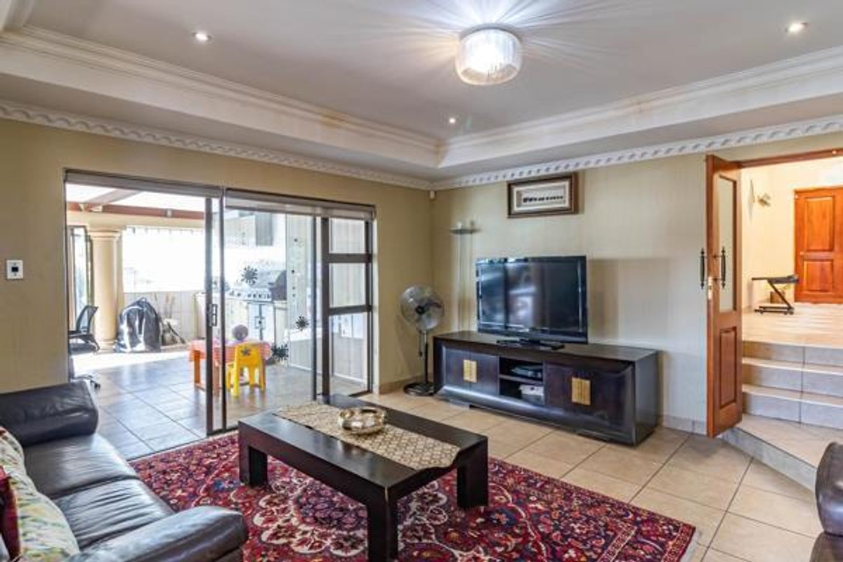 Spacious living room featuring recessed tray ceiling, tiled flooring, and large sliding glass doors providing seamless access to the covered patio area.