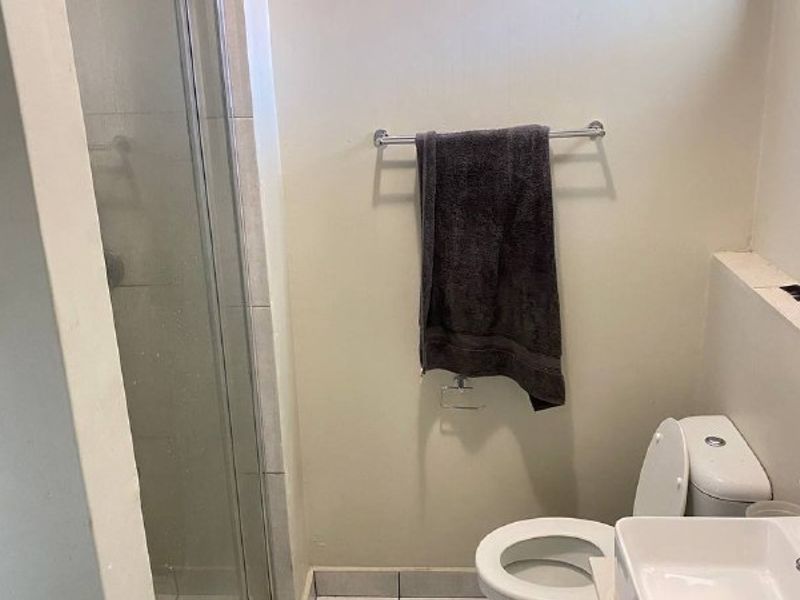 A functional bathroom featuring a shower enclosure, a wall-mounted basin, and a standard toilet, providing essential amenities in a compact layout.