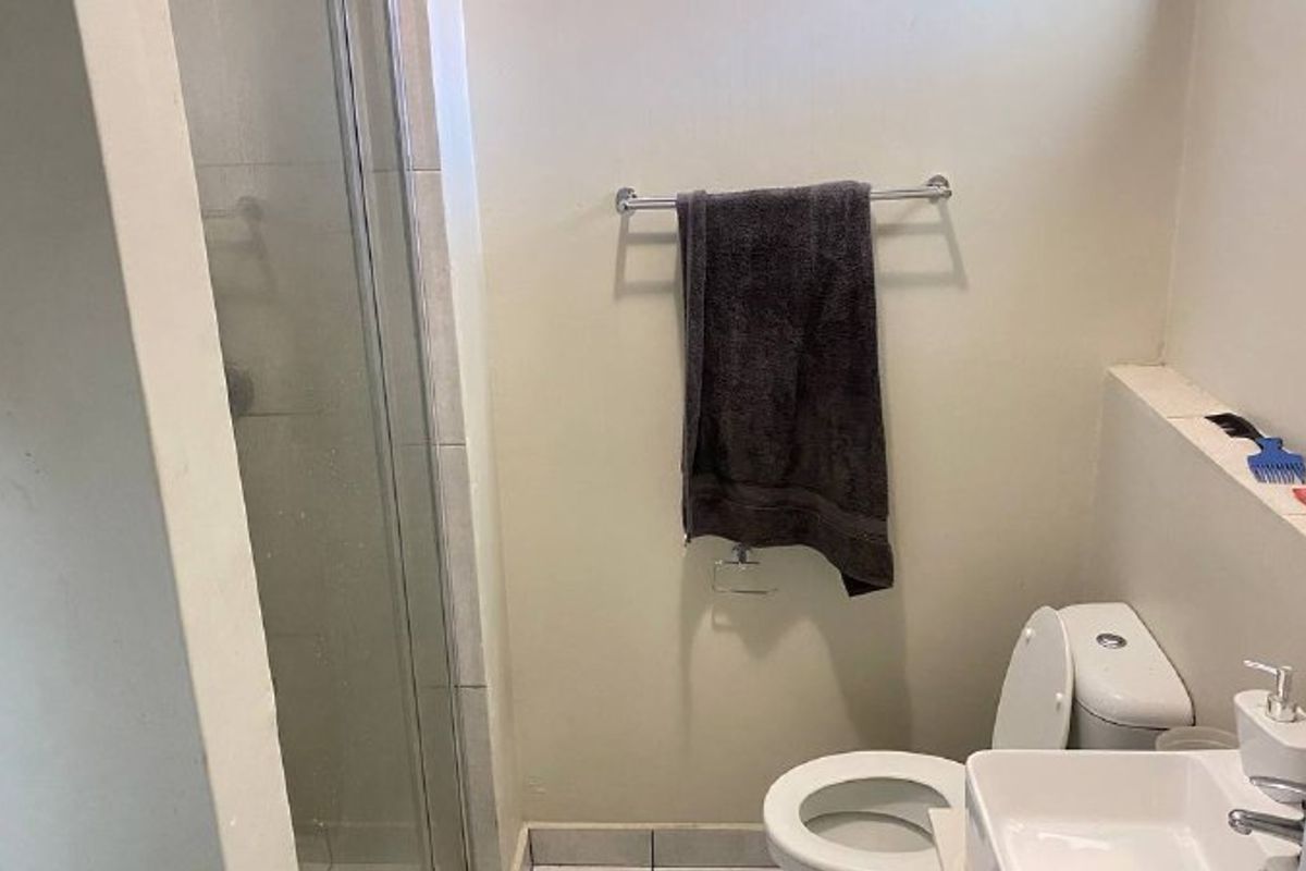 A functional bathroom featuring a shower enclosure, a wall-mounted basin, and a standard toilet, providing essential amenities in a compact layout.