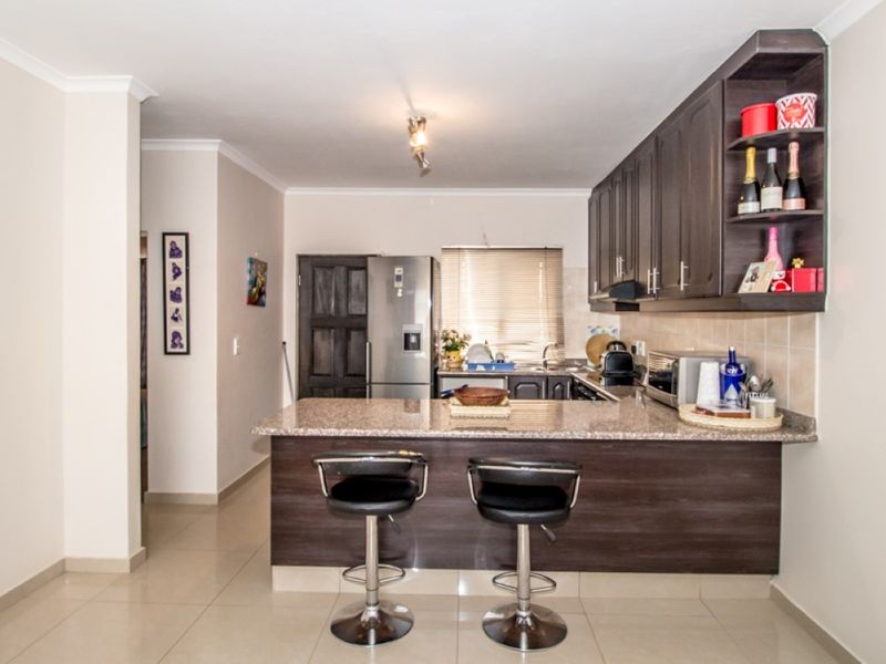 A functional kitchen featuring dark wood cabinetry, granite countertops, a breakfast bar, and tiled flooring, offering a clean and well-maintained workspace.