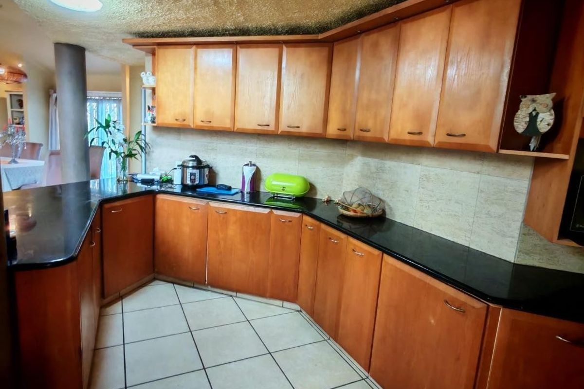 A functional kitchen featuring wooden cabinetry, dark granite countertops, and ceramic floor tiles, with a unique textured ceiling finish.