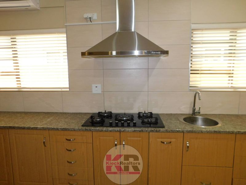 A functional kitchen featuring wooden cabinetry, granite countertops, a gas hob with a stainless steel extractor fan, and a tiled backsplash.