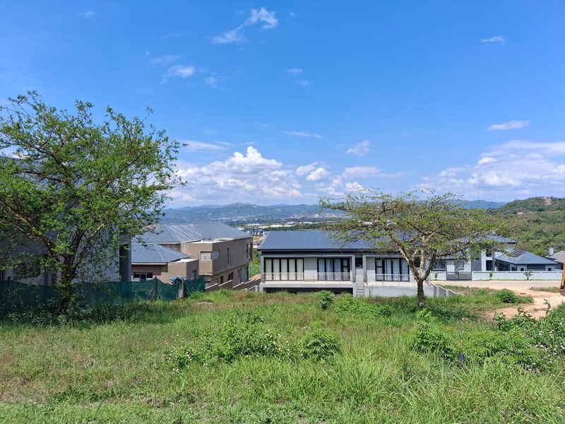 A scenic view overlooking a residential development with modern homes, set against a backdrop of distant hills and a clear blue sky.
