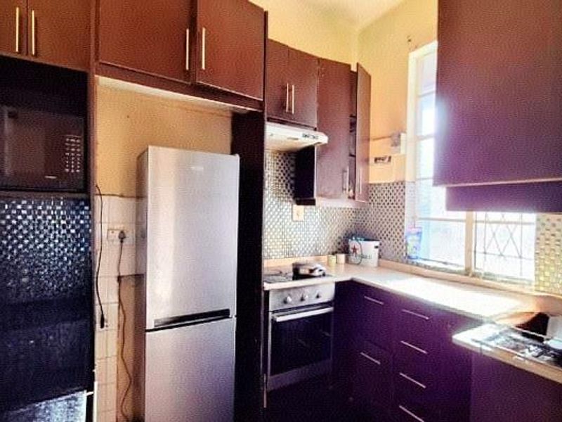 A compact kitchen featuring dark wood cabinetry, a built-in oven, hob, extractor fan, and a tiled backsplash with a window providing natural light.
